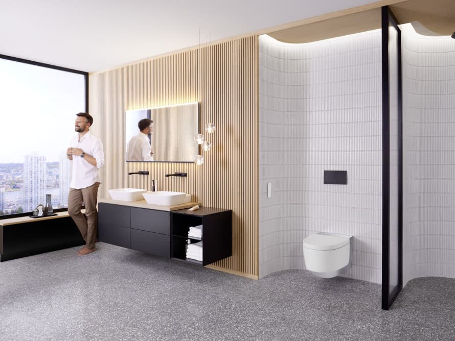 Homem numa casa de banho ampla com mobiliário escuro e sanita bidé Geberit AquaClean Homem numa casa de banho ampla com mobiliário escuro e sanita bidé Geberit AquaClean
